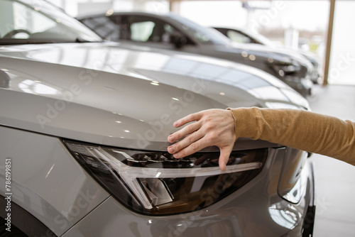Cropped view of hand of man buyer choosing auto, wants to buy new automobile. Customer touching car headlights in showroom vehicle salon dealership store. Sales concept.