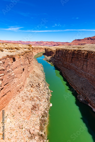 Colorado river gorge “Marble Canyon“ seen from famous Navajo Bridges near Page, Arizona (USA). Sunny desert scenery with red sandstone mountains, blue sky and green water. Colorful landscape with sun.