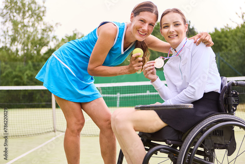 Celebration of triumph: Two athletes, one in a wheelchair, showcasing a gold medal on a tennis court photo