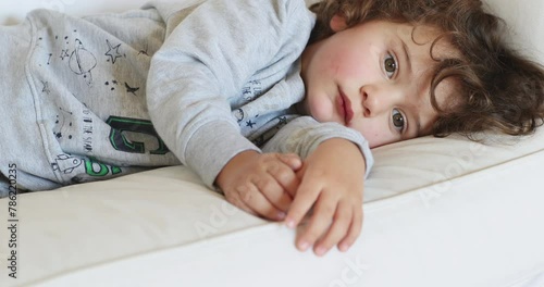 Young boy resting on a white sofa, looking unwell and tired photo