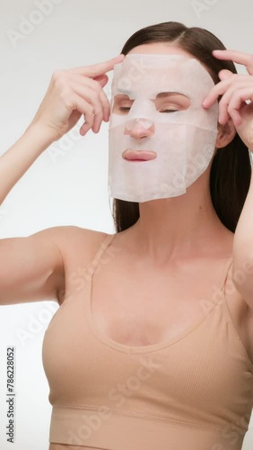 Beautiful brunette woman with clean skin applies a fabric face mask. Daily beauty routine (ID: 786228052)