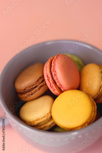 Purple cup filled with pastel macarons on pink background. Selective focus.