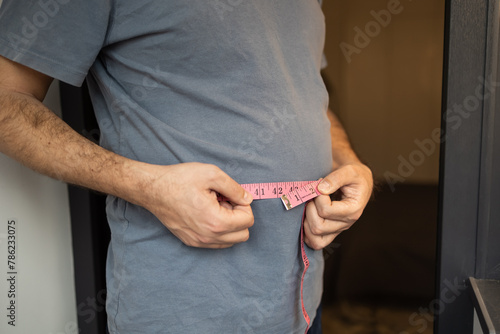Overweight man measures his waist with measuring tape. Fat belly visceral fat. Body mass index, grade 1 obesity, eating disorders and physical activity, excess high-calorie food or eating disorder