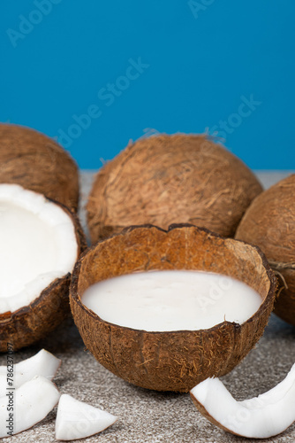 Coconut milk in coconut shell and half coconut, chopped flesh on a blue background