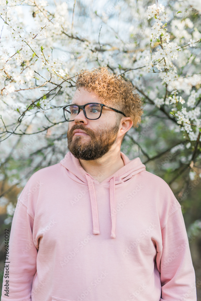 Male bearded man standing under branches with flowers of blooming almond or cherry tree in spring garden. Spring blossom. Male bearded man standing under branches with flowers of blooming almond or cherry tree in spring garden. Spring blossom.