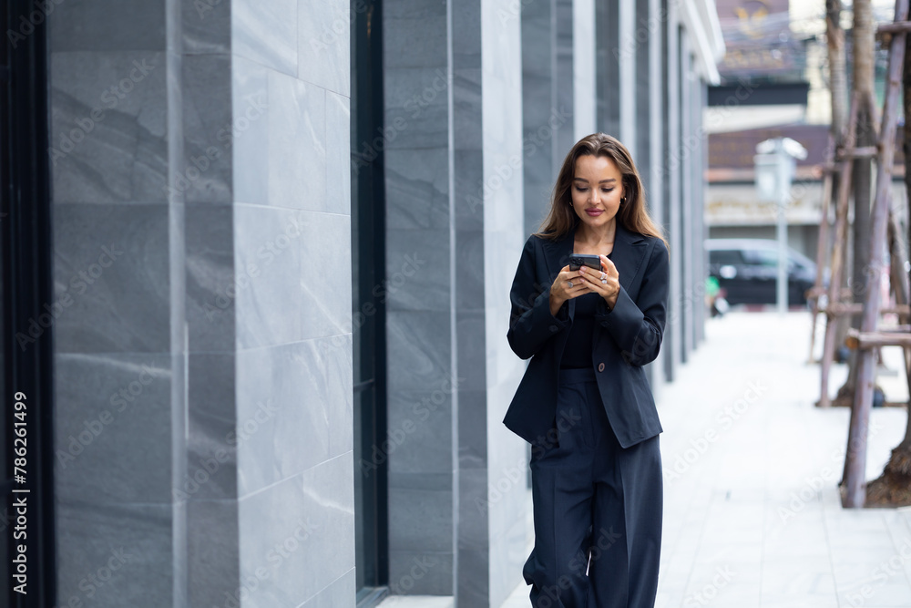 Mobile phone technology lifestyle - Hispanic business woman uses mobile phone device communicating with a colleague. Female walking outside modern office building