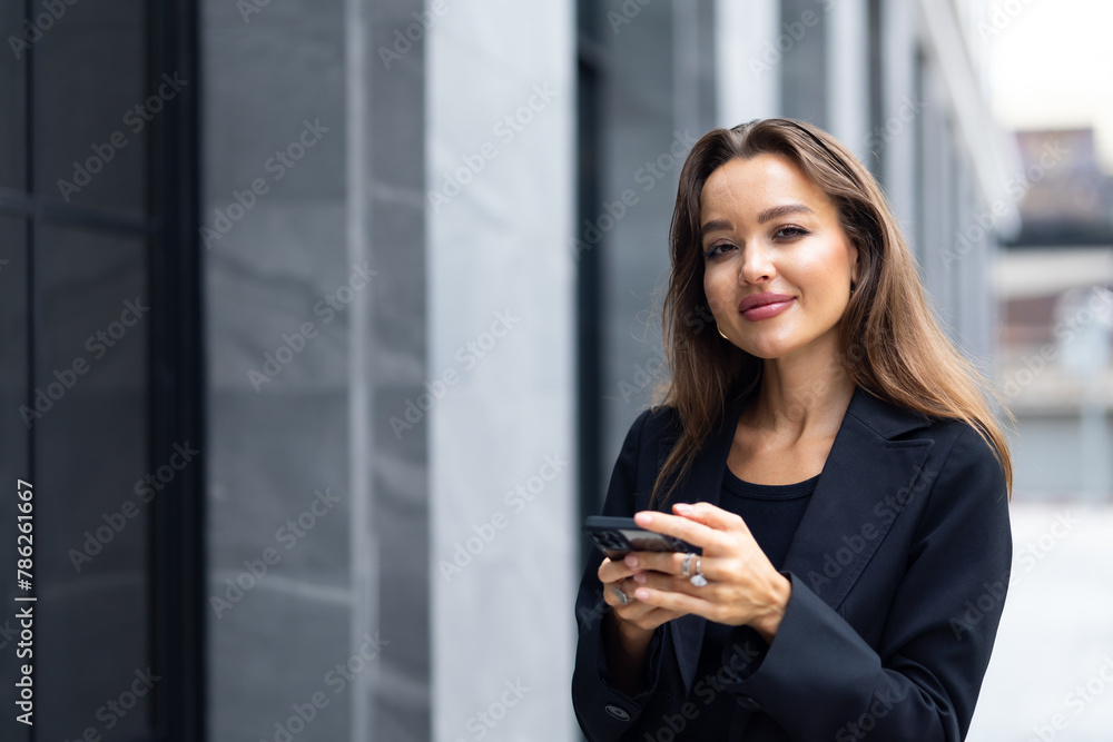 Mobile phone technology lifestyle - Hispanic business woman uses mobile phone device communicating with a colleague. Female walking outside modern office building