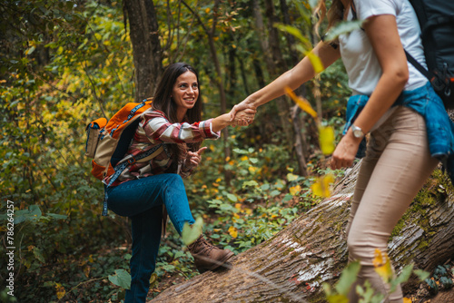 Happy women help while hiking up a rocky mountain in nature with backpack. Females friends exercise in nature park climbing and jumping while with sportswear training or trekking together outdoors