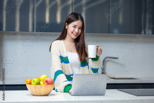 woman relaxing - Happy young teen girl using laptop computer sit at table working learning online in internet at home enjoy morning coffee in cozy house kitchen. Pretty woman wearing sweater at home
