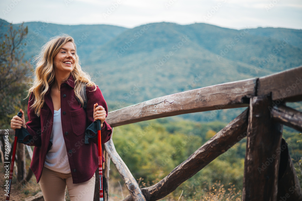 Front view of senior woman hiker standing outdoors in nature at sunset. Portrait of a happy woman hiker standing on the slope of mountain ridge against mountains, blue cloudy sky on background. Front view of senior woman hiker standing outdoors in nature at sunset. Portrait of a happy woman hiker standing on the slope of mountain ridge against mountains, blue cloudy sky on background.