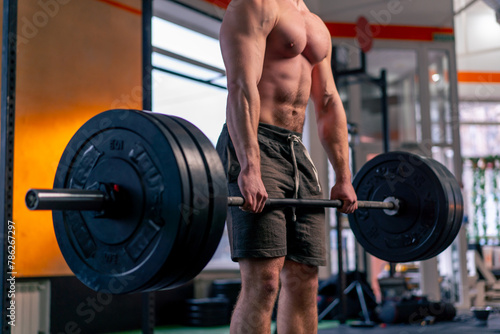 close up in a sports club a bald trainer in sports shorts lifts weights on a barbell