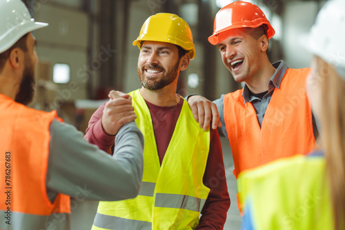 Attractive, happy, bearded, middle aged man wearing protective helmet shaking hands with colleagues