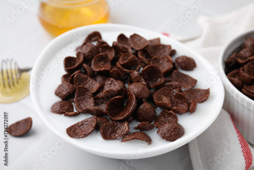 Breakfast cereal. Chocolate corn flakes and milk in bowl on white table, closeup