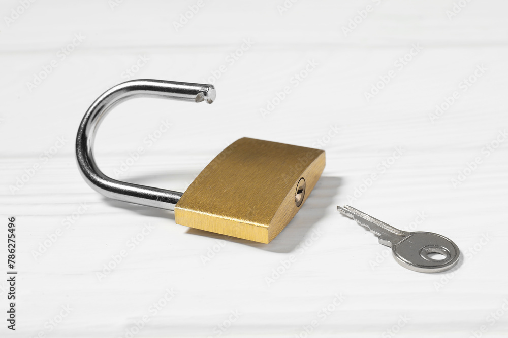 Steel padlock with key on white wooden table, closeup Steel padlock with key on white wooden table, closeup