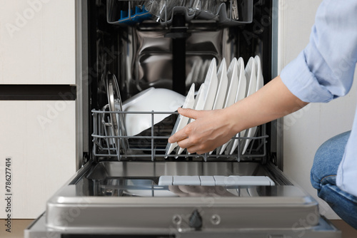 Woman loading dishwasher with plates indoors, closeup
