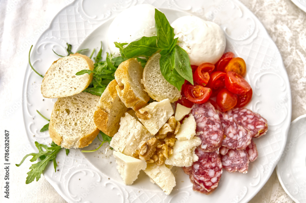 Traditional Italian food served on a plate, salami cheese, herbs, baguette, tomatoes