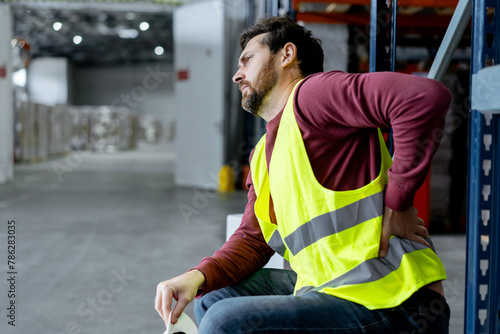 Upset, tired, overworked man, foreman wearing workwear touching back, having pain, spasm photo