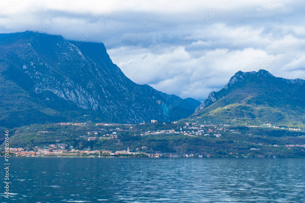 The largest Italian lake is Lake Garda in northern Italy. Small towns around a lake surrounded by cloud-covered Alps. Landscapes of Italy. The Alps towering over Europe. Overcast weather. Snowy peaks
