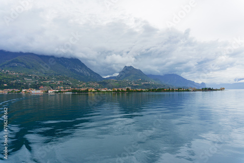 The largest Italian lake Garda in northern Italy. Small towns around a lake surrounded by cloud-covered Alps. Landscapes of Italy. The Alps towering over Europe. Overcast weather. Snowy peaks