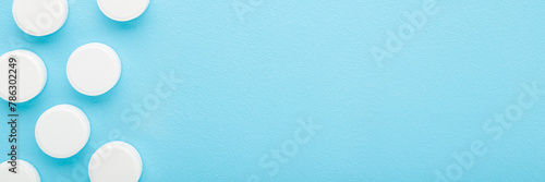 White pills of c vitamins on light blue table background. Pastel color. Closeup. Nutritional supplements. Wide banner. Empty place for text. Top down view.