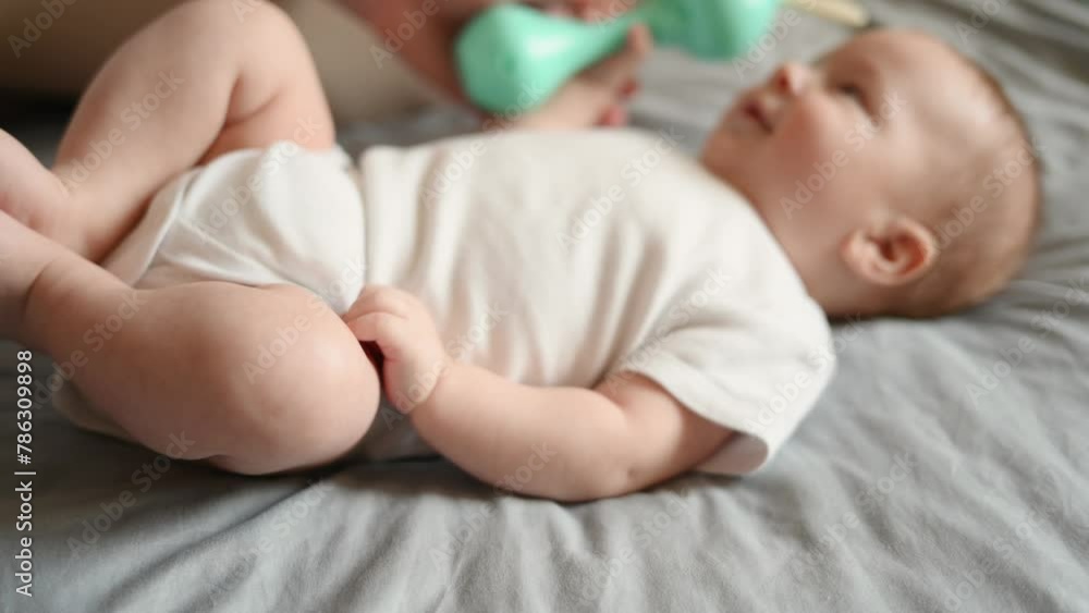 Infant lying on his back, awake, holding a rattle, playing with it, newborn baby smiling, soft focus, focus on legs. Concept of motherhood, maternity leave, child care, child development. Infant lying on his back, awake, holding a rattle, playing with it, newborn baby smiling, soft focus, focus on legs. Concept of motherhood, maternity leave, child care, child development.