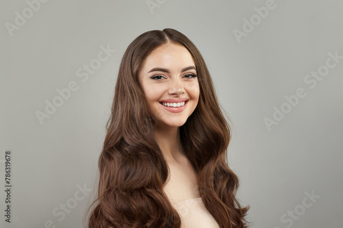Emotional young happy woman model with natural make-up, clean healthy fresh skin and long hair posing on gray background. Curly, haircare, skincare and facial treatment concept
