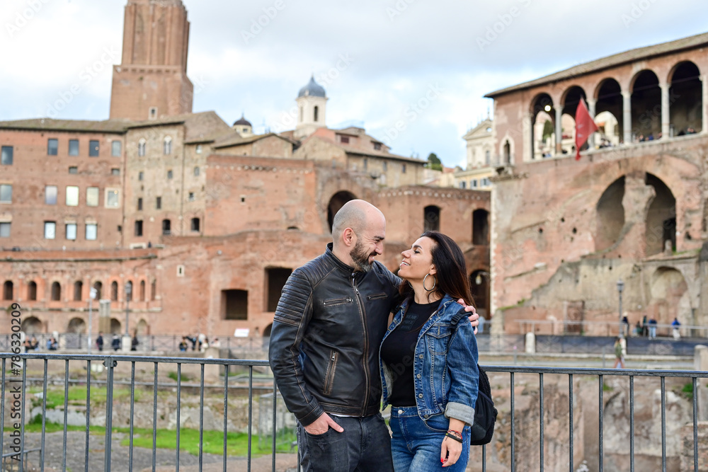 Happy  Beautiful Tourists  couple traveling at Rome, Italy,  near Ancient Trajan's Market, ruins in Via dei Fori Imperial Visiting Italy - man and woman enjoying weekend  weekend vacation 