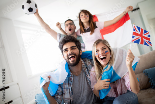 Diverse friends sports fans watching football match on TV at home. Celebrating shouting excited