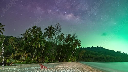 Night Timelapse of rising milky way behind palm trees and mountains with green light from fishing boat contaminated the dark sky at Koh Kood, a famous island in Trat, Thailand  photo
