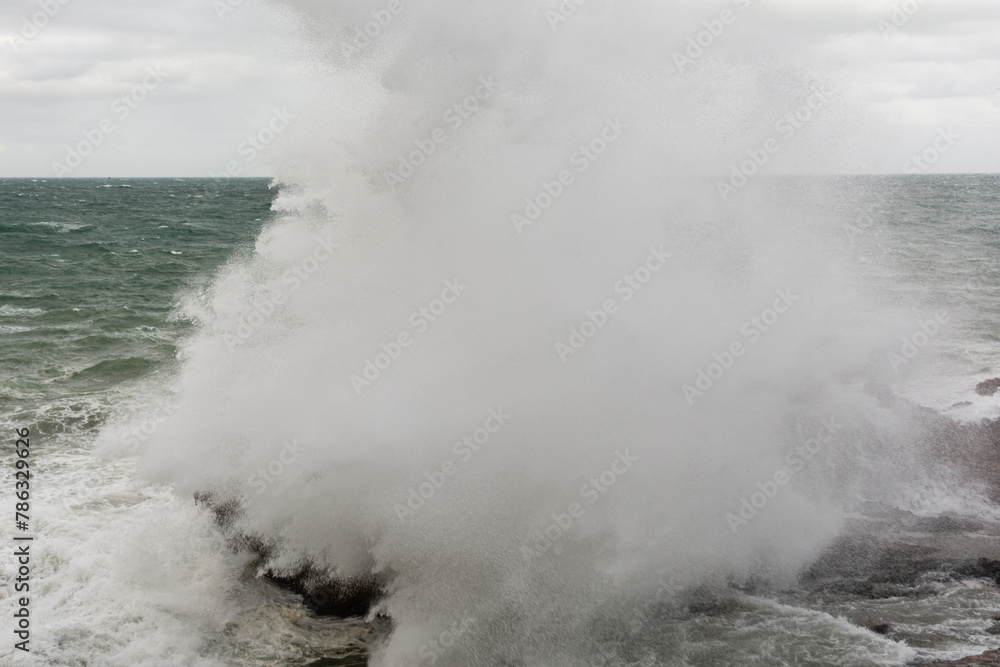 Fototapeta premium Immense waves hitting a large rock at the edge of the beach. Force of nature.