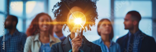 Individual holding a lighted bulb in front, concept of idea creation with peers in background photo
