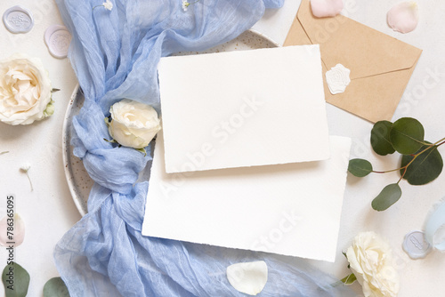 Cards near light blue tulle fabric knot and cream roses on plates top view copy space, wedding mockup