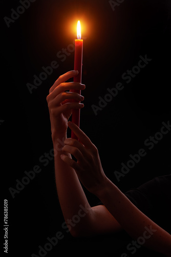 Woman’s hands holding red wax candle burning brightly on black