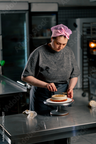 female baker in a professional kitchen distributes cream onto a sponge cake with a spatula