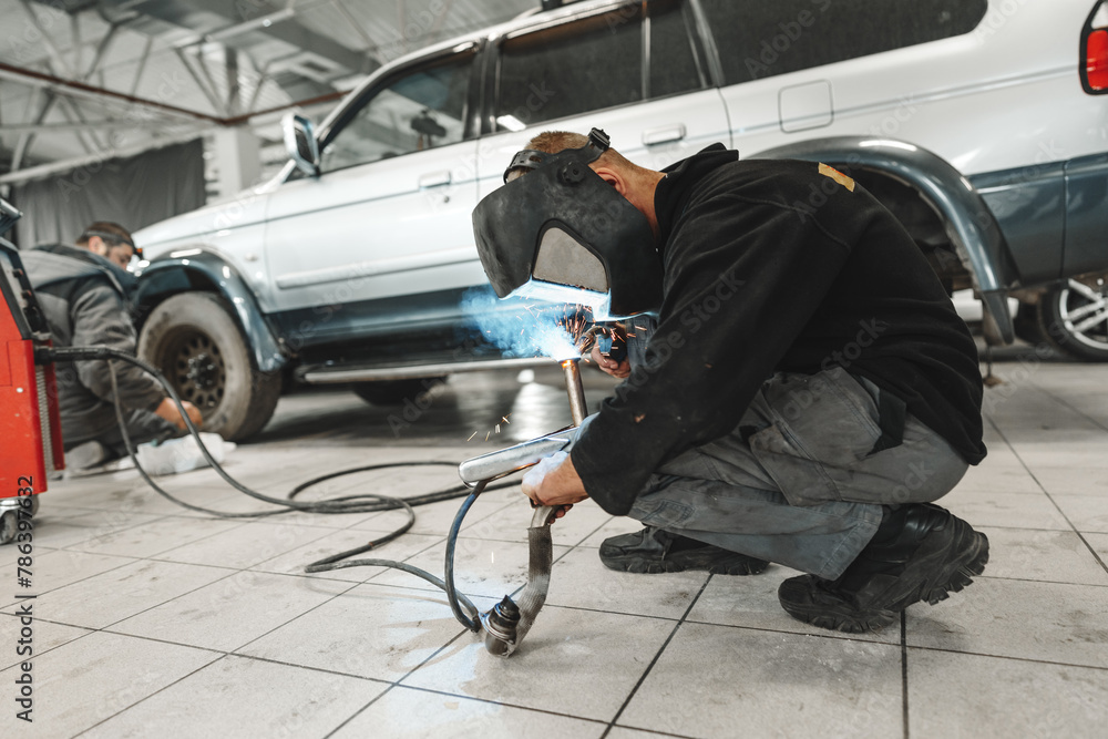 Welder in mask repairing detail in car service