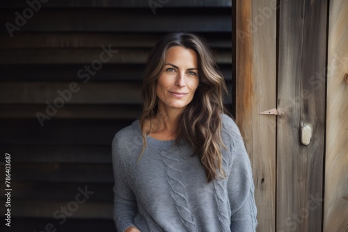 Portrait of a tender woman in her 40s wearing a cozy sweater on rustic wooden wall