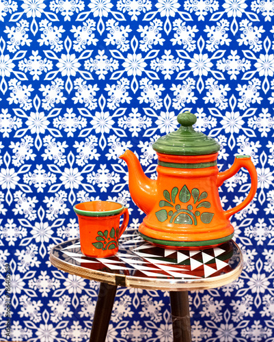 orange Teekanne und Tasse im Design der 70er vor einer blau gemusterten Tapete, retro