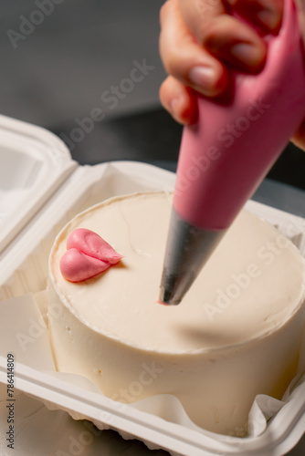 close-up of a female baker in a professional kitchen drawing a heart on a cake with pink cream