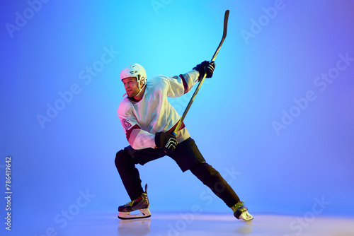 Canvas Print Man, hockey player wearing uniform and helmet, posing with stick against gradient blue background in neon light