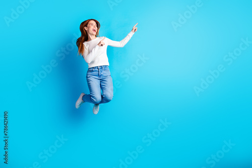 Full body photo of attractive young woman jump point look empty space dressed stylish white clothes isolated on blue color background
