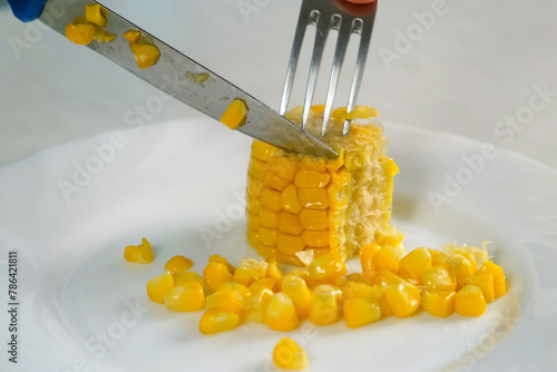 Woman cutting piece of baked corn on plate on kitchen at home, hand close-up. Prepare cook bake dish. Cuisine culinary nutrition domestic food recipe ingredients vegetable. Cooked sweet corn.
