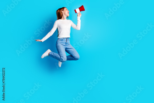Full body photo of attractive young woman jump hold megaphone dressed stylish white clothes isolated on blue color background