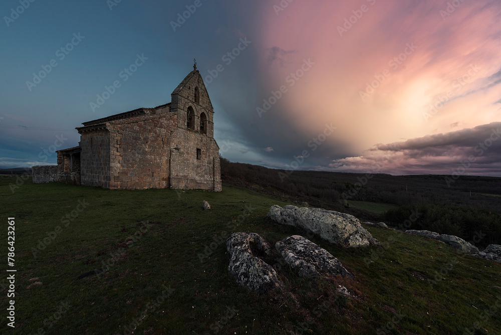 Sunset with dramatic sky in the Romanesque church of San Martín, in Quintanilla de la Berzosa, Aguilar de Campoo, Palencia, Castilla y León, with the tombs of the medieval necropolis in the foreground