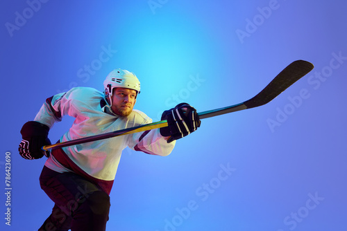 Photography Ambitious man, hockey player posing with stick, showing his determination against gradient blue background in neon light