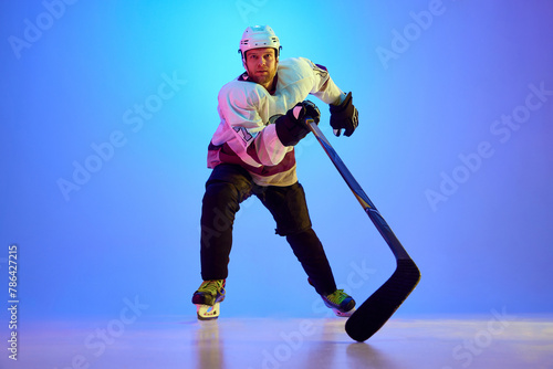 Photography Competitive and concentrated man, hockey player expressing readiness to win against gradient blue background in neon light