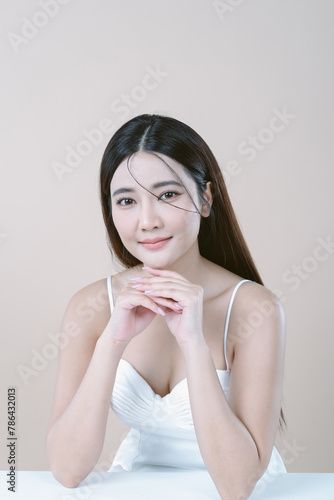 Sexy beautiful Asian woman in white dress with natural makeup and looking at camera isolated over beige background. Fashion shiny highlighter on skin, perfect make-up.