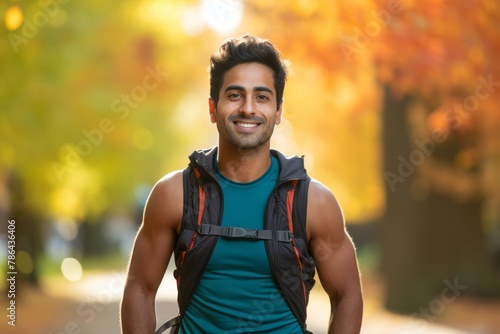 Portrait of a smiling indian man in his 20s wearing a lightweight running vest in background of autumn leaves