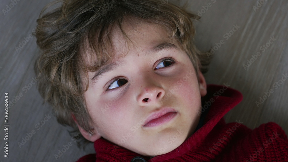 Close-Up Portrait of Thoughtful Child in Red Sweater Lying on Floor, Young Boy with Pensive expression Looks Upwards Close-Up Portrait of Thoughtful Child in Red Sweater Lying on Floor, Young Boy with Pensive expression Looks Upwards