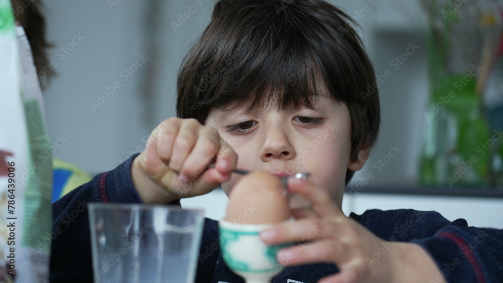 Child cracking open egg with spoon at breakfast table. One concentrated small boy opening soft-boiled egg with spoon Child cracking open egg with spoon at breakfast table. One concentrated small boy opening soft-boiled egg with spoon