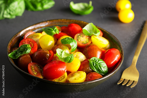 Bright juicy salad with colorful cherry tomatoes and aromatic basil leaves on black stone table close up. Healthy vegan food concept.
